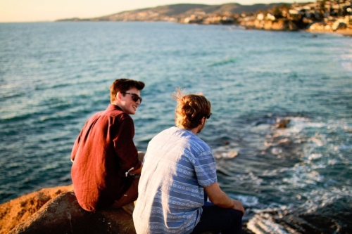 Two young men sitting on a rock overlooking the ocean talking